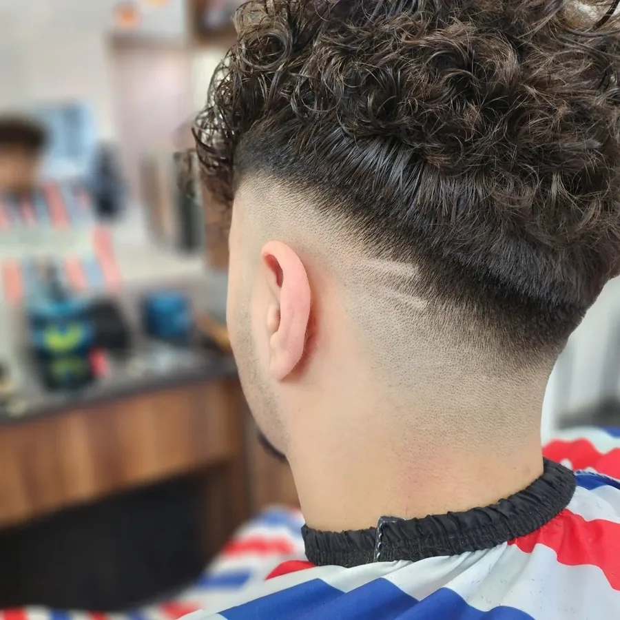 Lockiger Herrenhaarschnitt von hinten, im gestreiften Barber-Umhang.